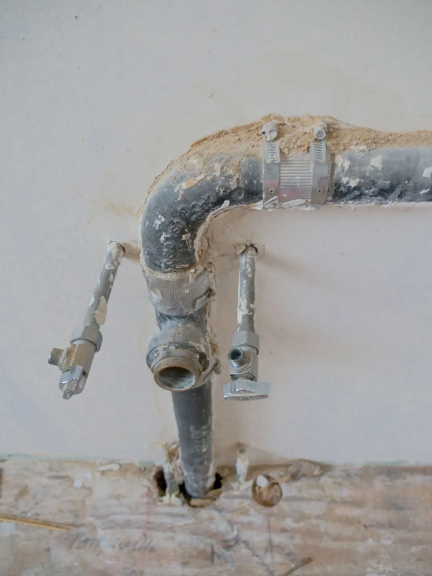 Aging galvanized supply pipes and chrome shutoff valves exposed in an opened wall