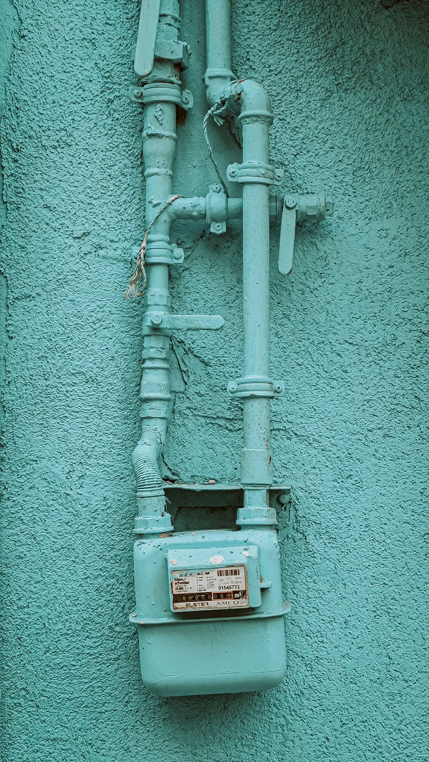 A residential gas meter and its supply piping mounted on an exterior stucco wall