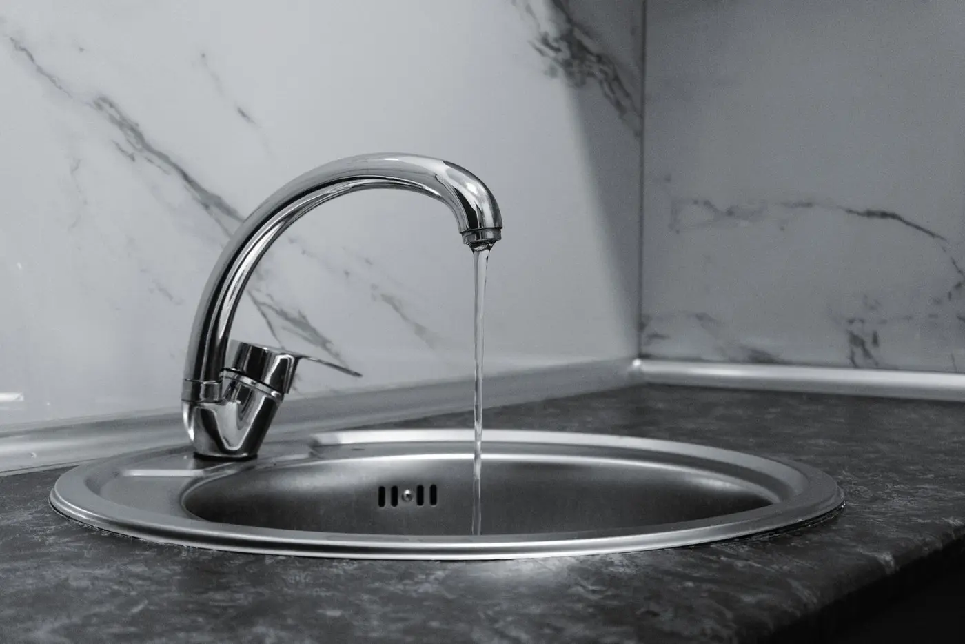 A chrome kitchen faucet running a steady stream of water into a stainless steel sink